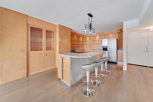 kitchen with light wood-type flooring, kitchen peninsula, stainless steel fridge, decorative light fixtures, and a breakfast bar area