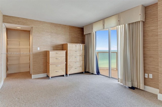 unfurnished bedroom featuring access to exterior, light colored carpet, and a water view