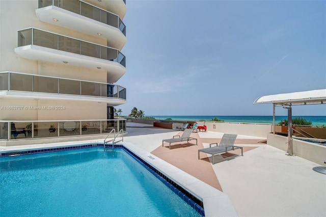 view of swimming pool with a patio area, a water view, and a beach view