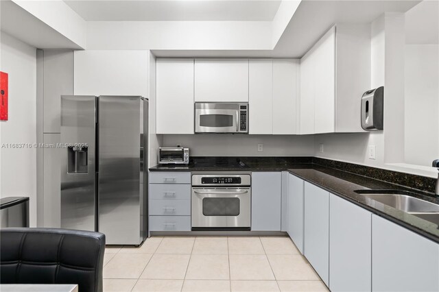 kitchen with sink, dark stone countertops, light tile patterned floors, appliances with stainless steel finishes, and white cabinets