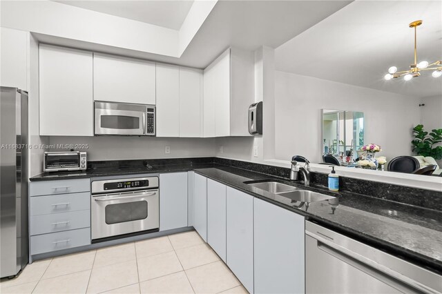 kitchen featuring sink, light tile patterned floors, appliances with stainless steel finishes, white cabinetry, and dark stone countertops