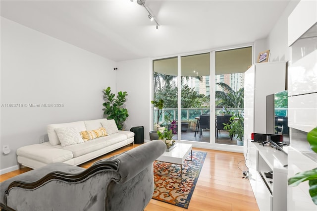 living room with a wall of windows, rail lighting, light wood-style flooring, and baseboards