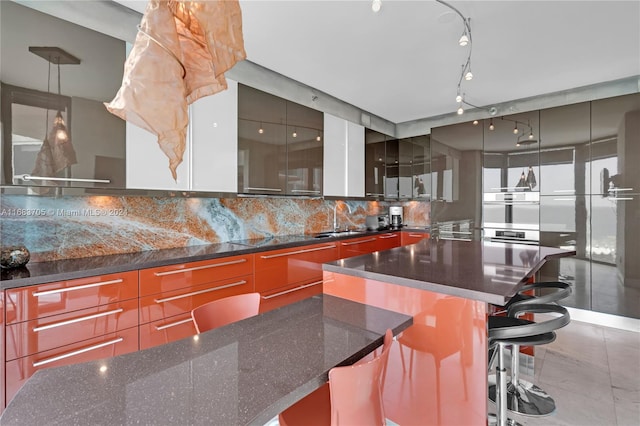 kitchen featuring a spacious island, a breakfast bar area, hanging light fixtures, backsplash, and sink