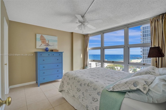 tiled bedroom featuring a textured ceiling, a water view, and ceiling fan