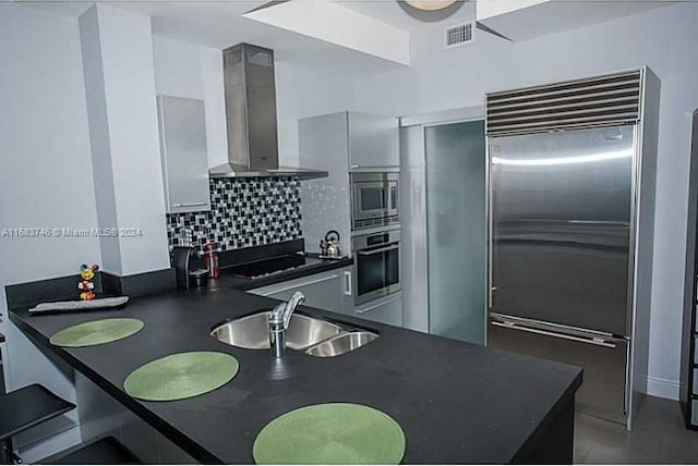 kitchen featuring wall chimney exhaust hood, tasteful backsplash, sink, and built in appliances