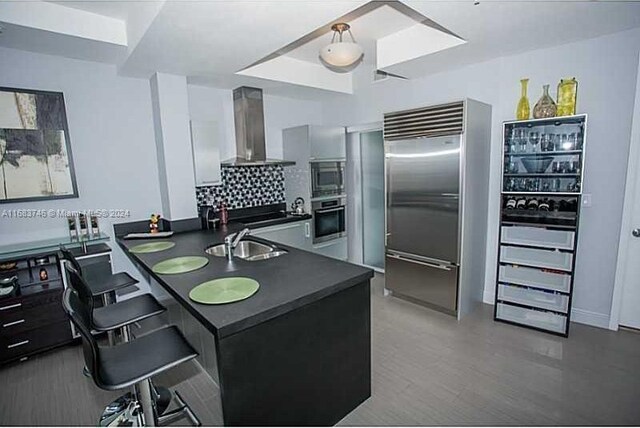 kitchen with a kitchen breakfast bar, wall chimney exhaust hood, built in appliances, and kitchen peninsula