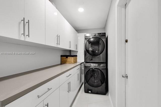 laundry area with stacked washer and clothes dryer, light tile patterned floors, and cabinets