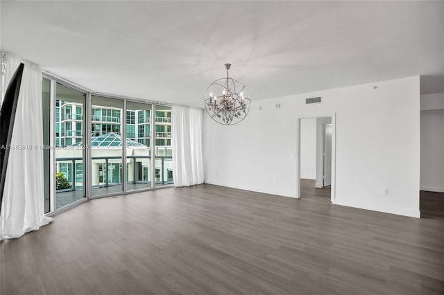 spare room featuring expansive windows, dark hardwood / wood-style flooring, and an inviting chandelier