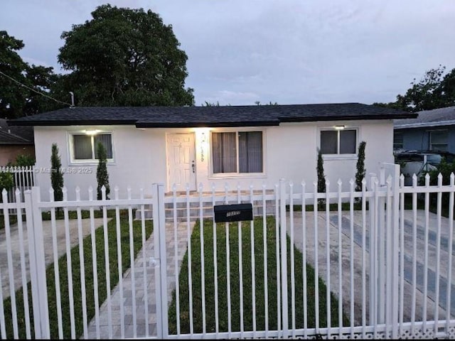 view of front facade featuring a fenced front yard, a shingled roof, and stucco siding