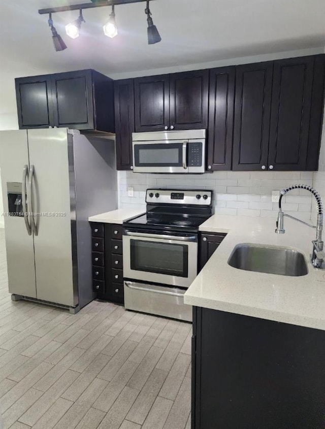 kitchen with light stone countertops, dark cabinets, a sink, stainless steel appliances, and backsplash
