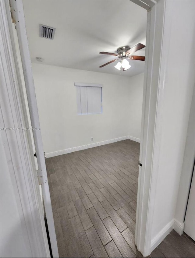 empty room featuring visible vents, baseboards, a ceiling fan, and dark wood finished floors
