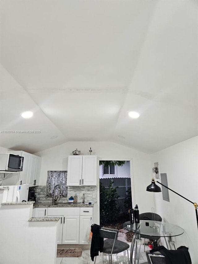 kitchen featuring tasteful backsplash, white cabinets, stainless steel microwave, light stone countertops, and lofted ceiling