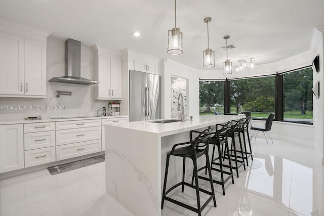 kitchen with wall chimney range hood, stainless steel refrigerator, and white cabinets