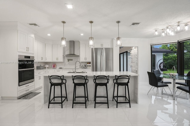 kitchen featuring wall chimney range hood, appliances with stainless steel finishes, sink, white cabinets, and a breakfast bar