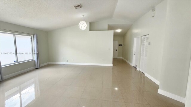 unfurnished room featuring lofted ceiling, light tile patterned floors, a textured ceiling, visible vents, and baseboards