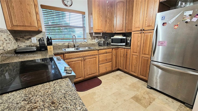 kitchen with appliances with stainless steel finishes, dark stone countertops, tasteful backsplash, and sink