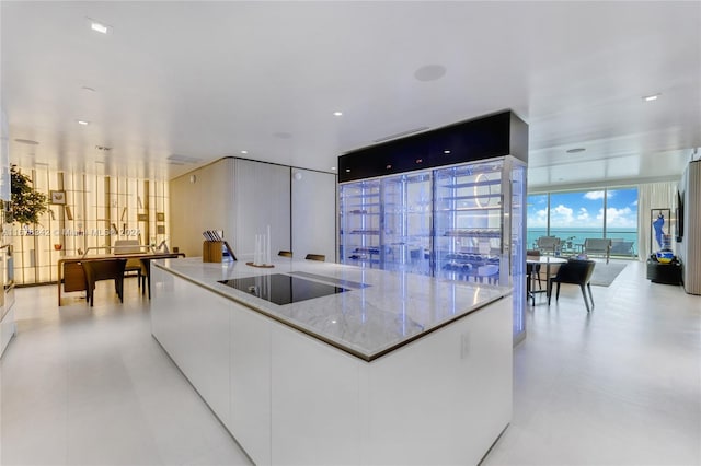 kitchen featuring black electric stovetop, white cabinetry, a large island, expansive windows, and light stone counters