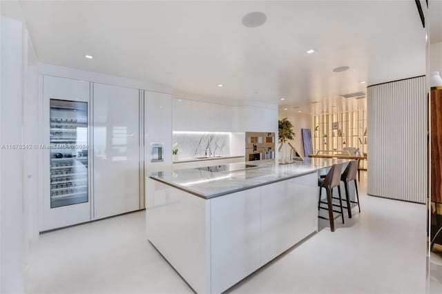 kitchen featuring a spacious island, light stone counters, black electric cooktop, and white cabinets