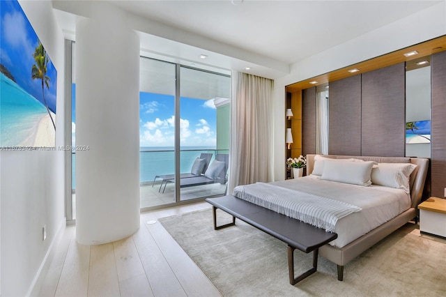 bedroom featuring access to exterior, a water view, light wood-type flooring, and expansive windows