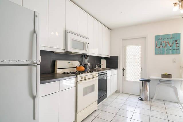 kitchen featuring white appliances, tasteful backsplash, white cabinetry, and light tile patterned floors