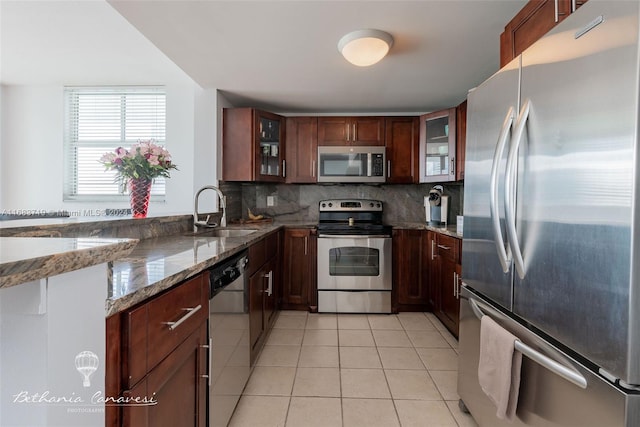 kitchen with tasteful backsplash, sink, stainless steel appliances, dark stone counters, and light tile patterned floors