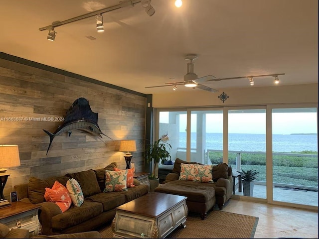 living room with wooden walls, a water view, track lighting, and ceiling fan