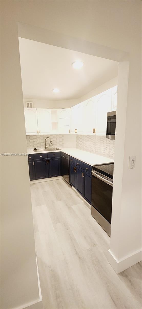 kitchen featuring white cabinetry, appliances with stainless steel finishes, light wood-type flooring, and decorative backsplash