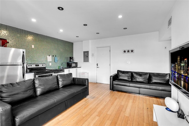 living room featuring electric panel, sink, and light wood-type flooring