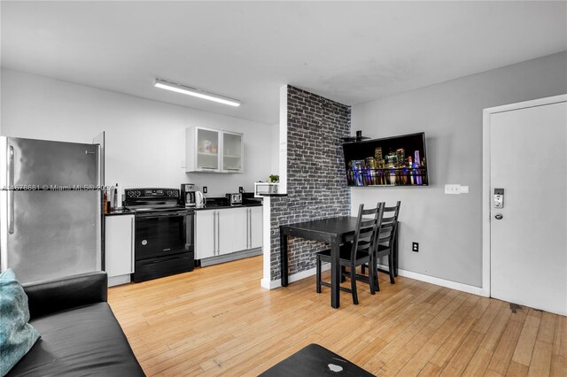 1512 Washington Ave Unit 203, Miami Beach, FL 33139 - kitchen featuring black range with electric stovetop, freestanding refrigerator, white cabinets, light wood-style flooring, and glass insert cabinets