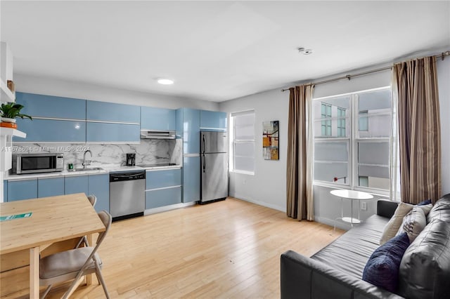 kitchen featuring stainless steel appliances, backsplash, sink, light wood-type flooring, and blue cabinetry