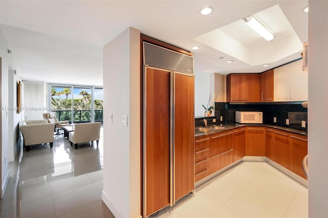 kitchen with paneled fridge, sink, backsplash, and light tile patterned floors