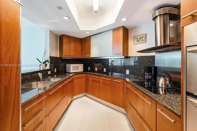 kitchen with black electric stovetop, sink, decorative backsplash, dark stone counters, and extractor fan