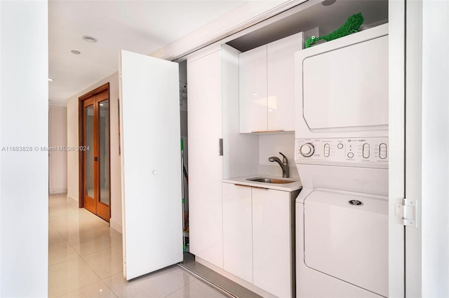 laundry room featuring sink, stacked washer / drying machine, cabinets, and light tile patterned floors