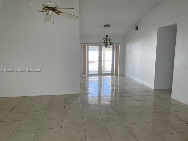 tiled empty room featuring ceiling fan with notable chandelier, high vaulted ceiling, and french doors