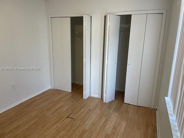 unfurnished bedroom with light hardwood / wood-style flooring and multiple closets