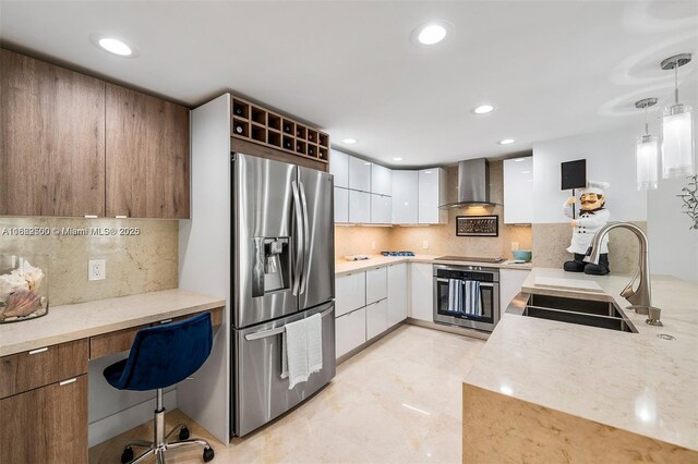 kitchen with wall chimney range hood, white cabinets, appliances with stainless steel finishes, sink, and decorative light fixtures