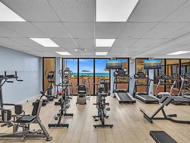 exercise room with a paneled ceiling, floor to ceiling windows, and hardwood / wood-style floors