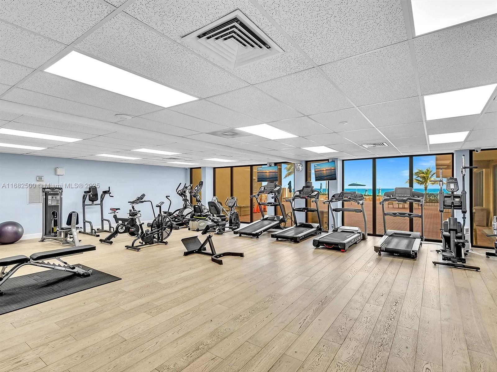 exercise room with a drop ceiling, wood-type flooring, and expansive windows