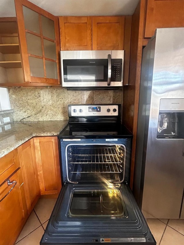 kitchen with light tile patterned floors, light stone countertops, backsplash, and appliances with stainless steel finishes