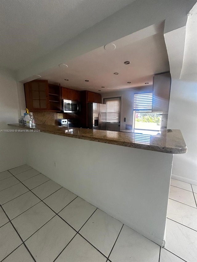 kitchen featuring stone counters, light tile patterned floors, tasteful backsplash, kitchen peninsula, and stainless steel appliances