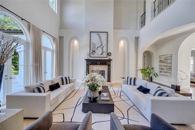 living room with a high end fireplace, light hardwood / wood-style flooring, a towering ceiling, and plenty of natural light