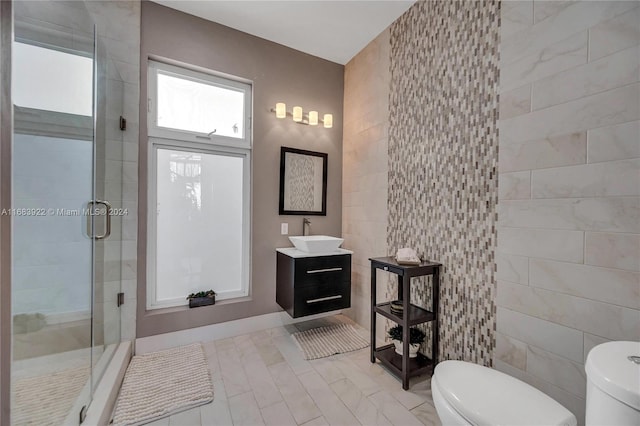 bathroom featuring a shower with door, vanity, toilet, and tile walls