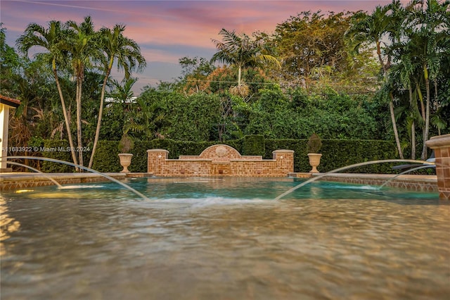 pool at dusk featuring a hot tub and pool water feature