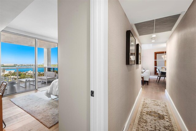 corridor with a water view, wood-type flooring, and floor to ceiling windows