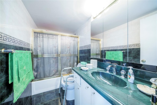 full bathroom with tile patterned floors, toilet, vanity, bath / shower combo with glass door, and tile walls