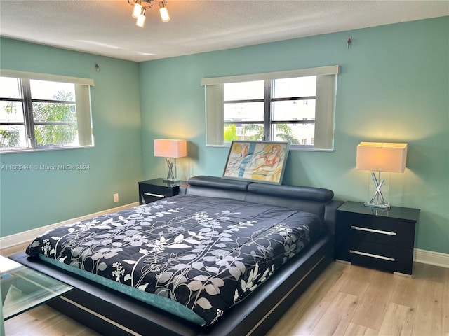 bedroom with a textured ceiling, multiple windows, and light wood-type flooring