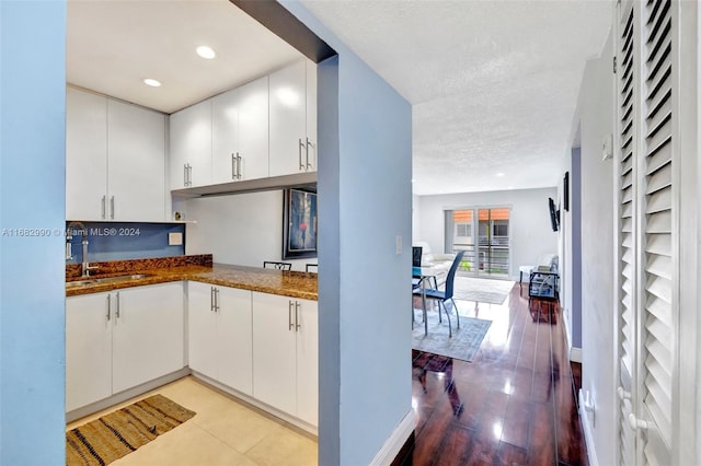 kitchen with sink, light hardwood / wood-style flooring, a textured ceiling, and white cabinetry