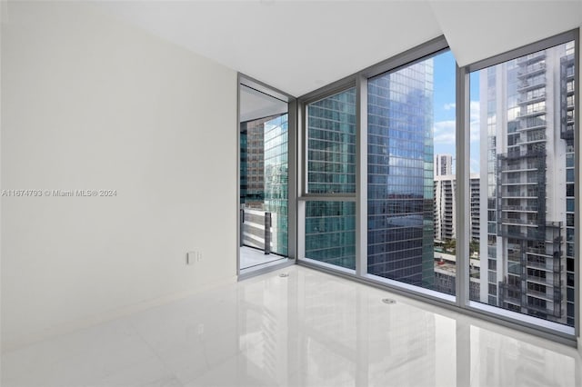 spare room with a healthy amount of sunlight, tile patterned flooring, and a wall of windows