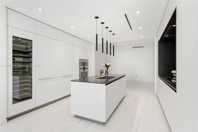 kitchen with sink, hanging light fixtures, white cabinetry, wine cooler, and a kitchen island with sink