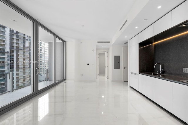 interior space with dark countertops, modern cabinets, a sink, white cabinetry, and backsplash